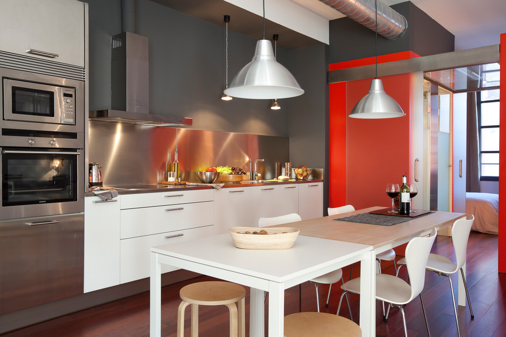 Inspiration for a mid-sized industrial single-wall open plan kitchen in Barcelona with flat-panel cabinets, white cabinets, metallic splashback, stainless steel appliances, no island, dark hardwood floors, stainless steel benchtops and metal splashback.