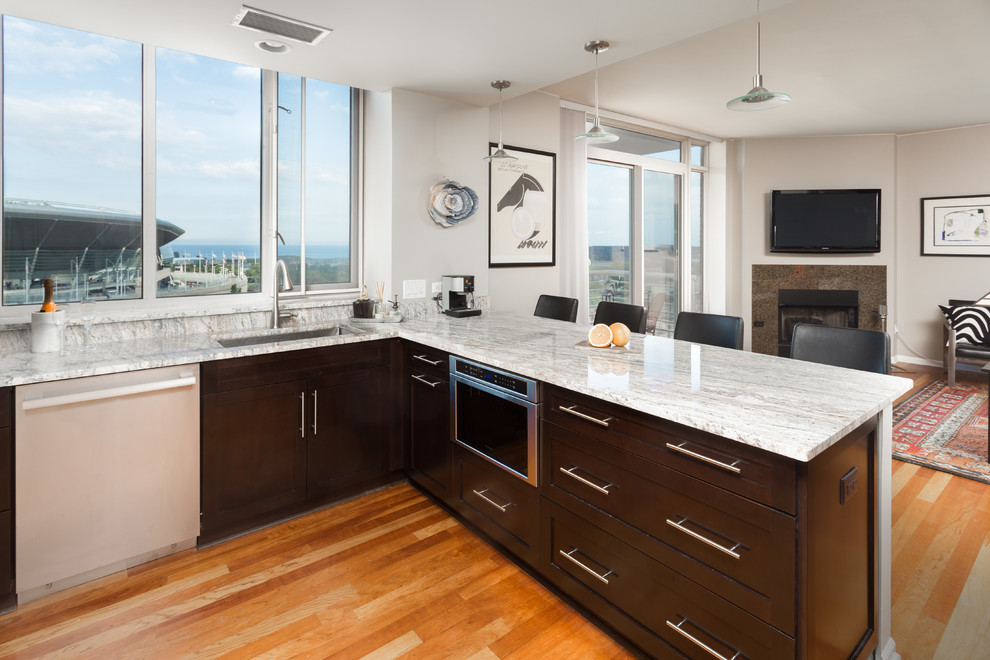 Inspiration for a mid-sized transitional u-shaped medium tone wood floor open concept kitchen remodel in Chicago with an undermount sink, shaker cabinets, dark wood cabinets, white backsplash, stainless steel appliances, a peninsula, marble countertops and subway tile backsplash