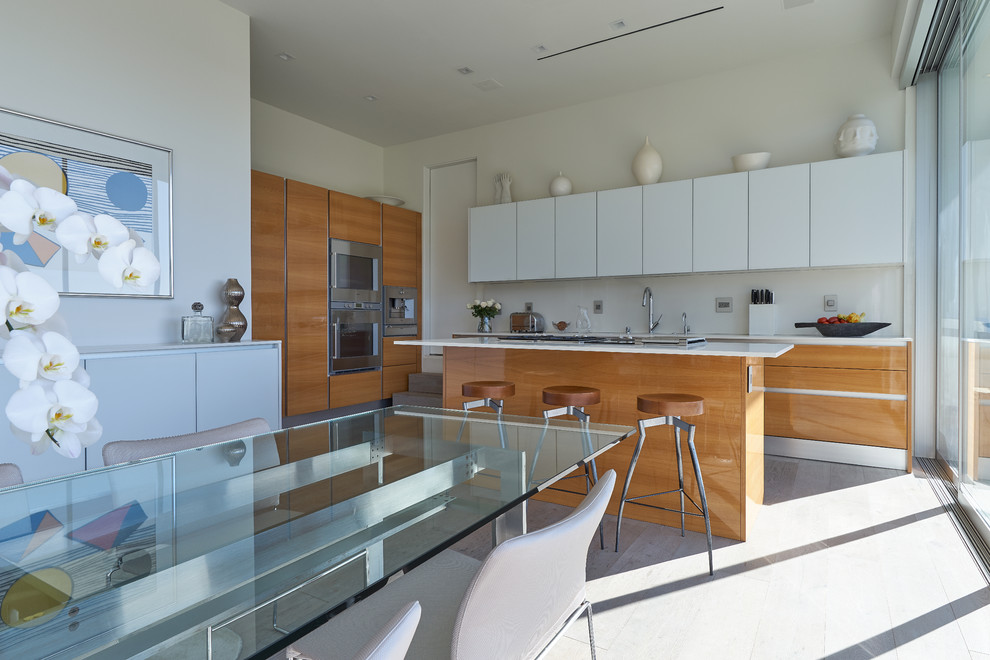 Photo of a mid-sized modern galley open plan kitchen in Los Angeles with an undermount sink, flat-panel cabinets, light wood cabinets, quartz benchtops, white splashback, stone slab splashback, stainless steel appliances, light hardwood floors, with island, yellow floor and white benchtop.