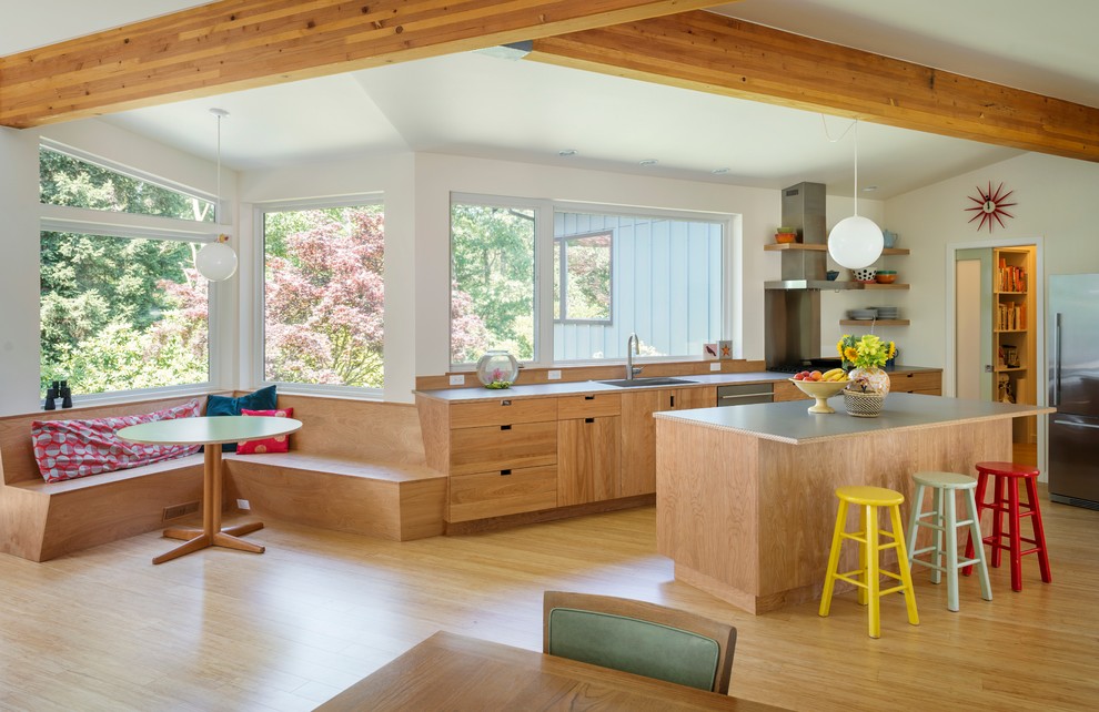 Design ideas for a midcentury l-shaped open plan kitchen in Seattle with with island, flat-panel cabinets, medium wood cabinets, laminate benchtops, stainless steel appliances, a drop-in sink and medium hardwood floors.