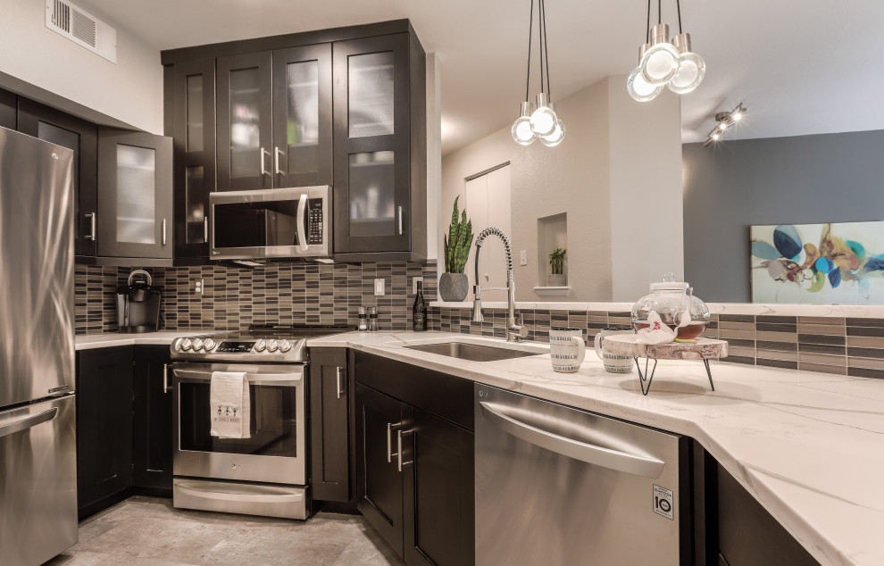 Photo of a small contemporary kitchen in Denver with a single-bowl sink, shaker cabinets, black cabinets, quartz benchtops, grey splashback, glass tile splashback, stainless steel appliances, vinyl floors, no island, grey floor and white benchtop.