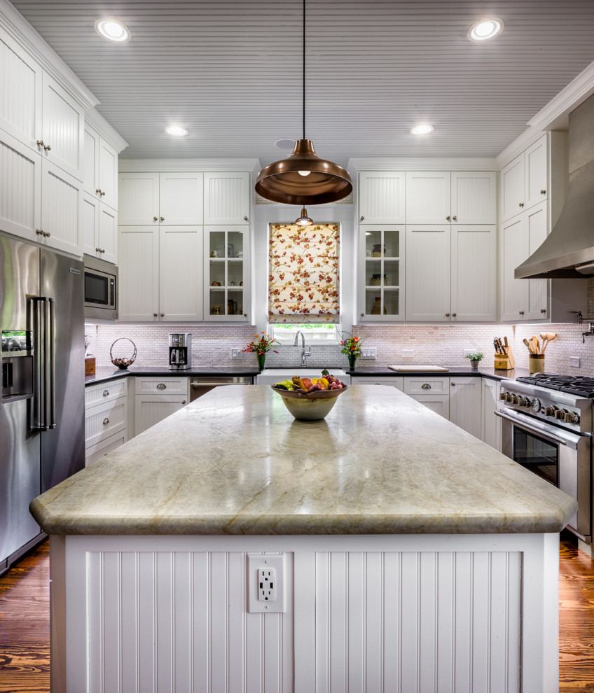 Design ideas for a traditional u-shaped kitchen in Houston with a farmhouse sink, shaker cabinets, white cabinets, white splashback, mosaic tile splashback, stainless steel appliances, medium hardwood floors, with island, brown floor and black benchtop.