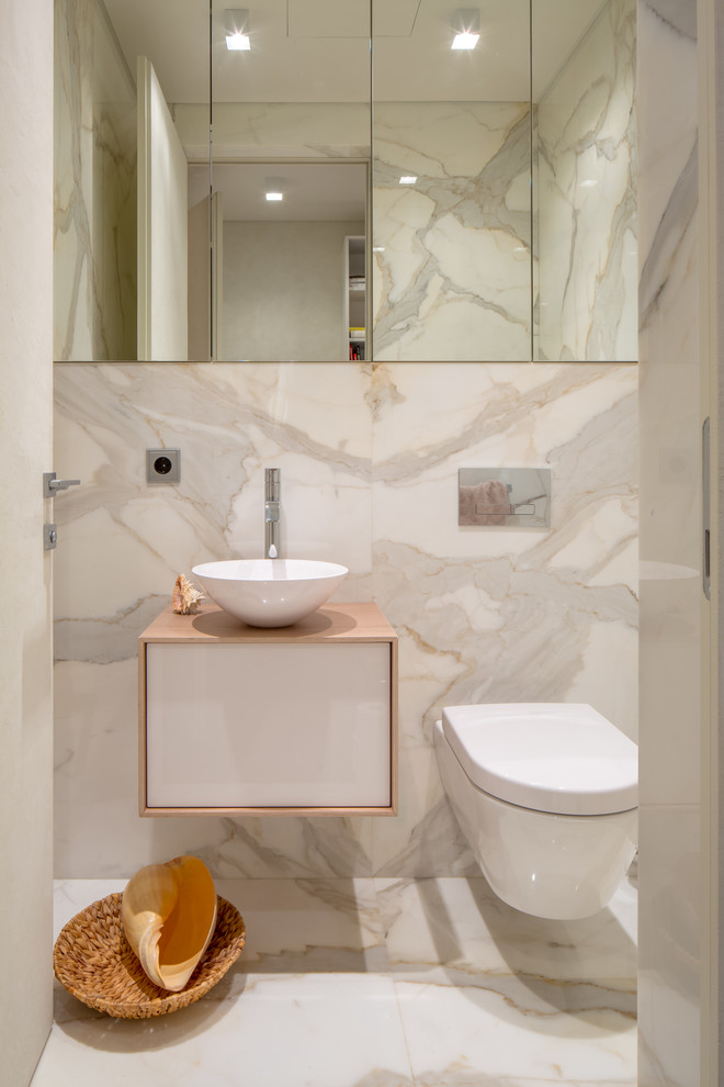 Photo of a contemporary powder room in Moscow with flat-panel cabinets, white cabinets, a wall-mount toilet, white walls, marble floors, a vessel sink, white floor, marble and beige benchtops.
