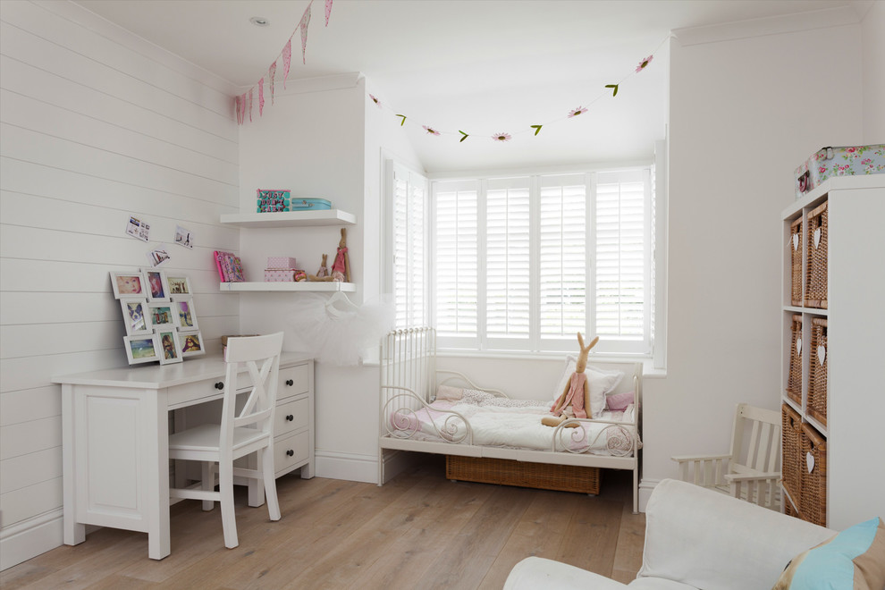 Design ideas for a beach style kids' room for girls in London with white walls and light hardwood floors.