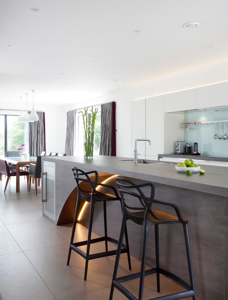 Inspiration for an expansive contemporary u-shaped open plan kitchen with an integrated sink, flat-panel cabinets, white cabinets, engineered stone countertops, green splashback, glass sheet splashback, stainless steel appliances, ceramic flooring and an island.
