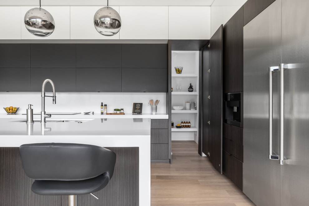 Photo of a mid-sized modern l-shaped kitchen in Vancouver with flat-panel cabinets, black cabinets, quartzite benchtops, white splashback, white benchtop, multiple islands, an undermount sink, engineered quartz splashback, stainless steel appliances, medium hardwood floors and brown floor.