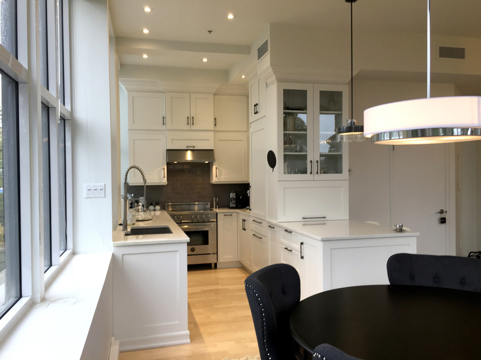 Photo of a small traditional u-shaped eat-in kitchen in Montreal with a triple-bowl sink, shaker cabinets, white cabinets, quartz benchtops, grey splashback, cement tile splashback, stainless steel appliances, light hardwood floors and no island.