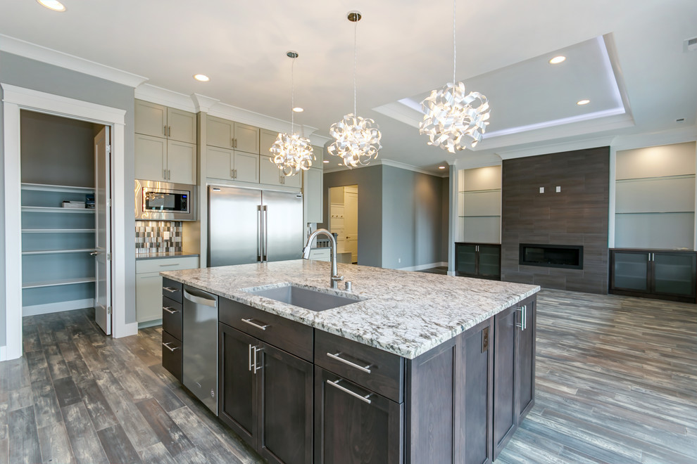 This is an example of a large transitional l-shaped open plan kitchen in Seattle with an undermount sink, grey cabinets, granite benchtops, multi-coloured splashback, mosaic tile splashback, stainless steel appliances, medium hardwood floors, with island and recessed-panel cabinets.