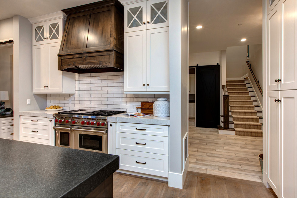 This is an example of a large country single-wall open plan kitchen in Salt Lake City with a farmhouse sink, shaker cabinets, white cabinets, soapstone benchtops, white splashback, subway tile splashback, stainless steel appliances, medium hardwood floors and with island.