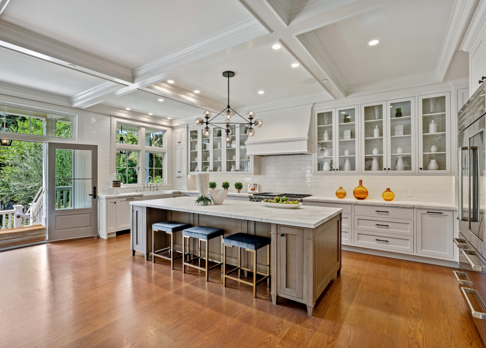 Photo of a medium sized classic grey and white u-shaped open plan kitchen in San Francisco with a belfast sink, shaker cabinets, white cabinets, marble worktops, white splashback, metro tiled splashback, stainless steel appliances, medium hardwood flooring, an island, brown floors, white worktops, a coffered ceiling and a feature wall.