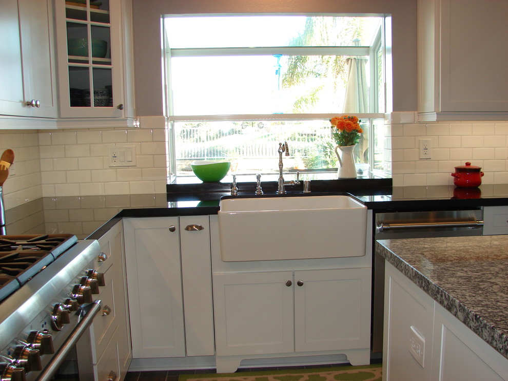 This is an example of a mid-sized transitional u-shaped eat-in kitchen in Orange County with a farmhouse sink, shaker cabinets, white cabinets, granite benchtops, white splashback, subway tile splashback, stainless steel appliances, porcelain floors and with island.