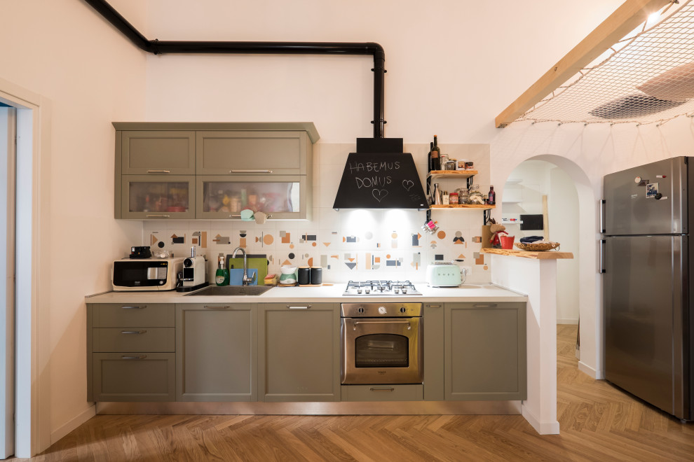 Photo of a small eclectic single-wall open plan kitchen in Rome with a drop-in sink, glass-front cabinets, green cabinets, laminate benchtops, multi-coloured splashback, porcelain splashback, stainless steel appliances, light hardwood floors, no island and white benchtop.