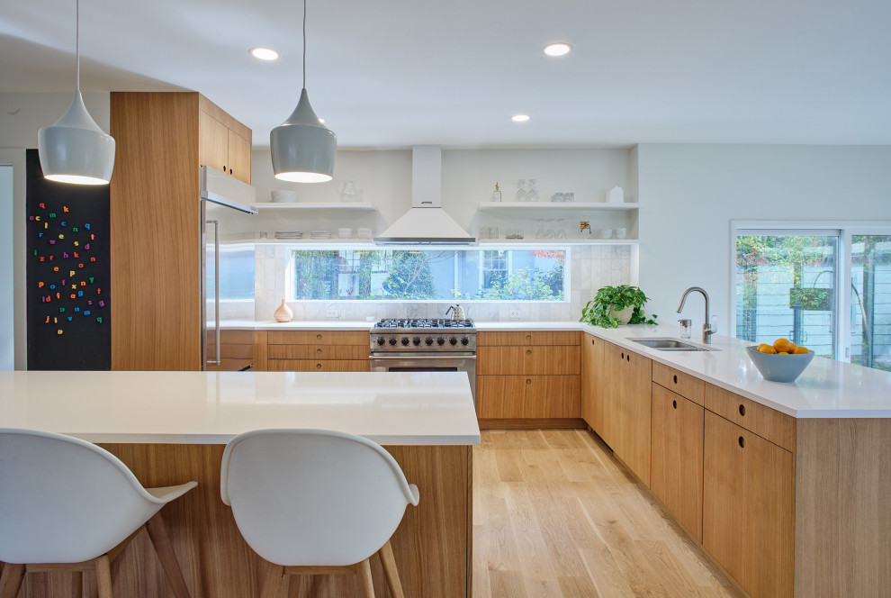 Inspiration for a scandinavian l-shaped eat-in kitchen in New York with an undermount sink, flat-panel cabinets, light wood cabinets, quartz benchtops, white splashback, marble splashback, stainless steel appliances, light hardwood floors, a peninsula and white benchtop.