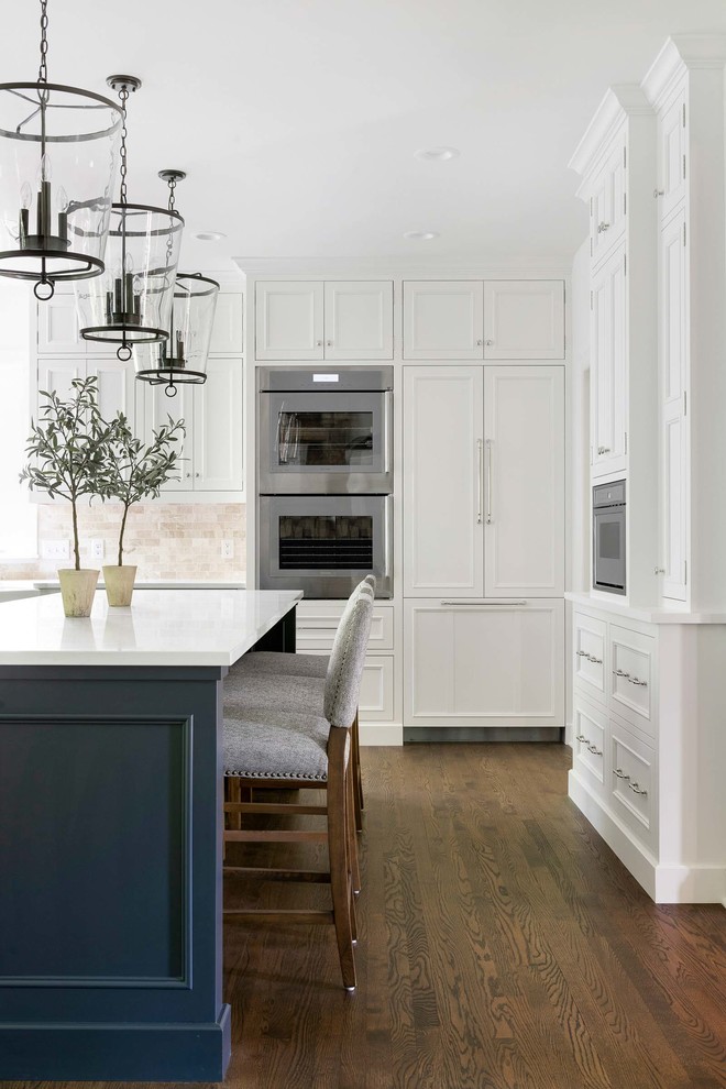 Country u-shaped eat-in kitchen in Minneapolis with a farmhouse sink, beaded inset cabinets, white cabinets, white splashback, dark hardwood floors, with island, brown floor and white benchtop.