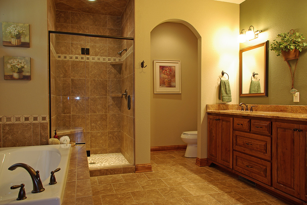 This is an example of a mid-sized traditional master bathroom in Milwaukee with raised-panel cabinets, medium wood cabinets, a drop-in tub, an alcove shower, a one-piece toilet, beige tile, yellow walls, stone tile, travertine floors, an undermount sink and engineered quartz benchtops.