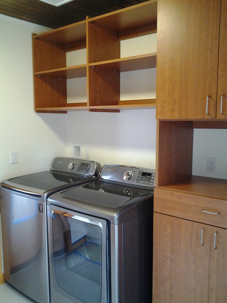 Photo of a small contemporary galley dedicated laundry room in Seattle with flat-panel cabinets, medium wood cabinets, white walls, vinyl floors and a side-by-side washer and dryer.