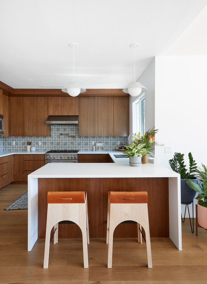Inspiration for a contemporary u-shaped kitchen in Los Angeles with an undermount sink, flat-panel cabinets, medium wood cabinets, multi-coloured splashback, stainless steel appliances, medium hardwood floors, a peninsula, brown floor and white benchtop.