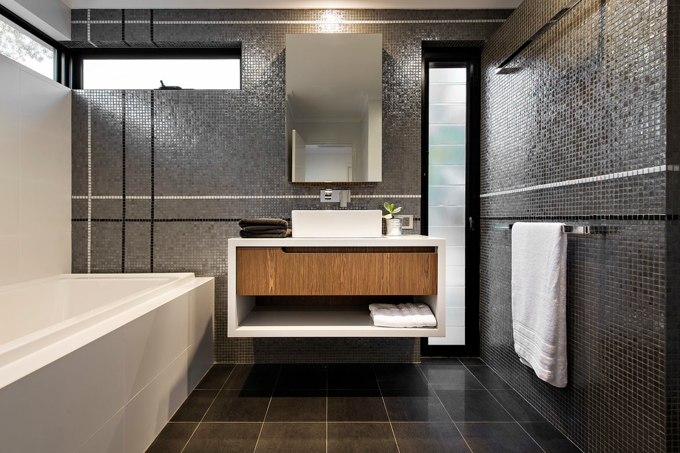 Design ideas for a mid-sized contemporary bathroom in Perth with a vessel sink, flat-panel cabinets, a drop-in tub, black tile, mosaic tile, black walls and porcelain floors.