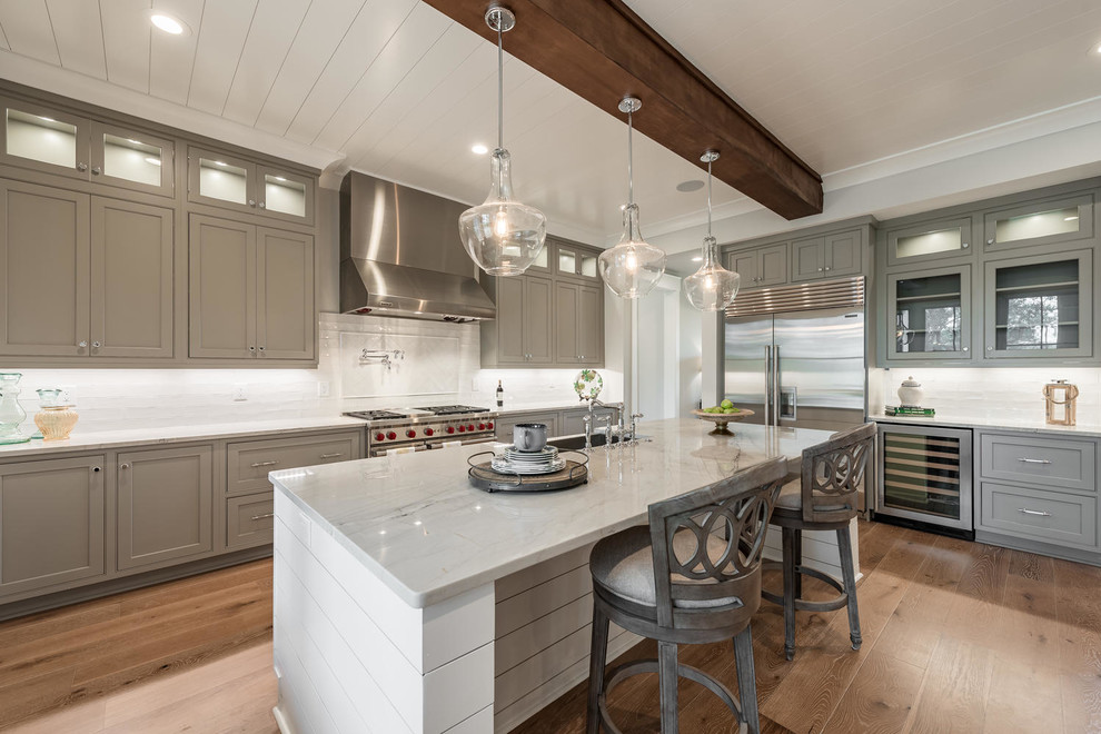 Transitional l-shaped kitchen in Charleston with an undermount sink, shaker cabinets, grey cabinets, white splashback, stainless steel appliances, light hardwood floors, with island and brown floor.