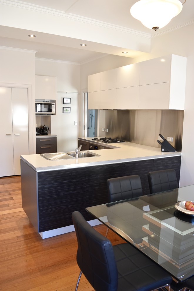 Inspiration for a small modern l-shaped eat-in kitchen in Sydney with a single-bowl sink, flat-panel cabinets, grey cabinets, laminate benchtops, metallic splashback, metal splashback, stainless steel appliances, medium hardwood floors and a peninsula.