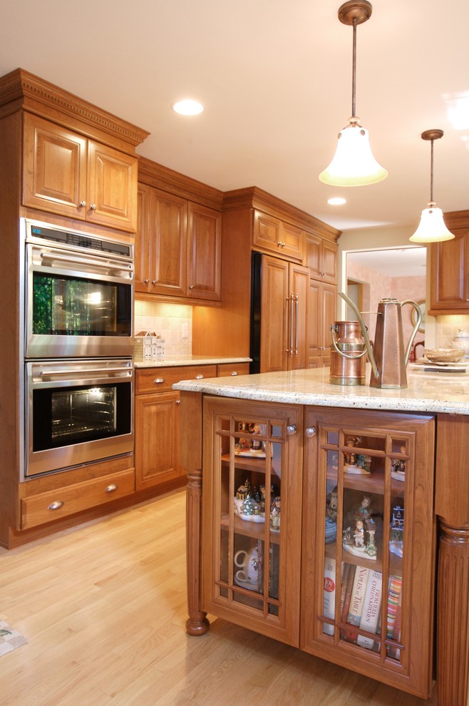 Photo of a traditional l-shaped eat-in kitchen in New York with an undermount sink, raised-panel cabinets, medium wood cabinets, granite benchtops, beige splashback, stone tile splashback and black appliances.