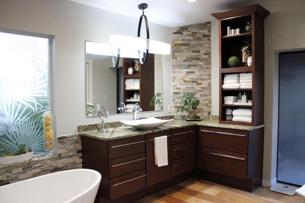 Photo of a large tropical master bathroom in Tampa with flat-panel cabinets, dark wood cabinets, a freestanding tub, stone tile, grey walls, light hardwood floors, a vessel sink, granite benchtops, a corner shower, beige tile, brown tile, gray tile, multi-coloured tile and a two-piece toilet.