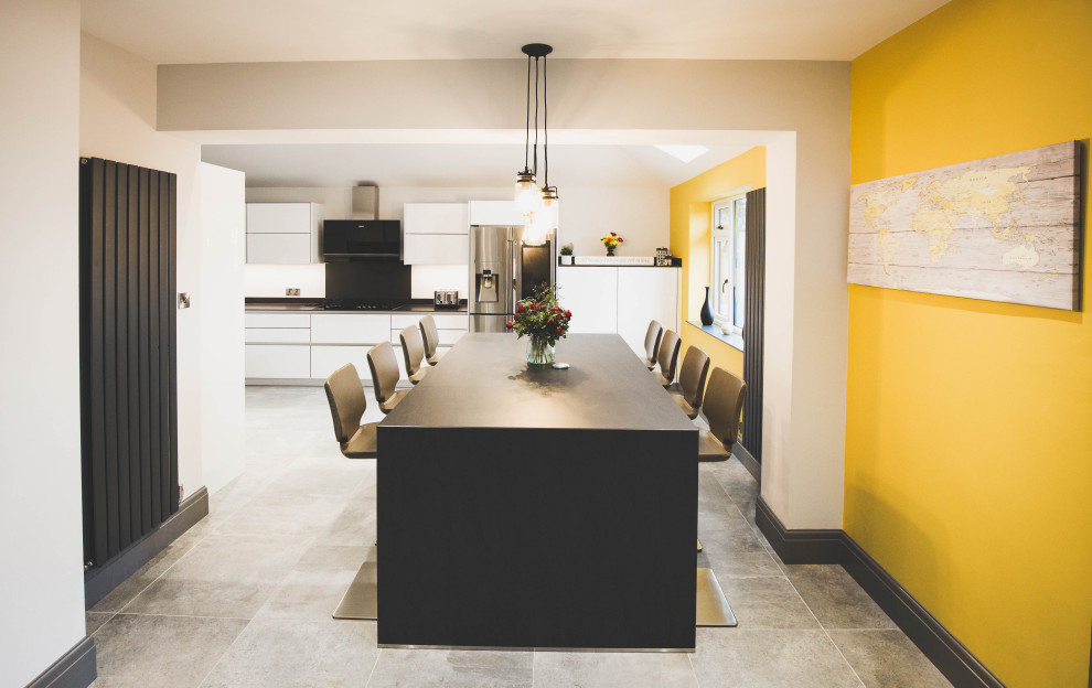 На фото: большая п-образная кухня в современном стиле с обеденным столом, монолитной мойкой, плоскими фасадами, желтыми фасадами, столешницей из кварцита, черной техникой, островом, серым полом, серой столешницей и акцентной стеной