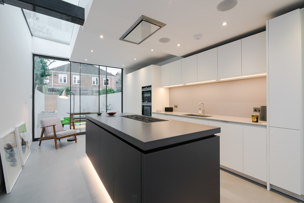 This is an example of a mid-sized contemporary galley eat-in kitchen in London with an undermount sink, flat-panel cabinets, black cabinets, solid surface benchtops, beige splashback, glass sheet splashback, stainless steel appliances, concrete floors, with island and grey floor.