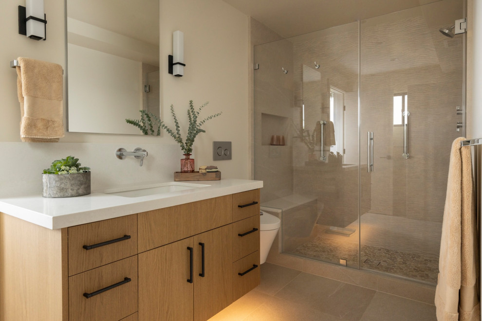 Example of a trendy beige tile beige floor and single-sink alcove shower design in San Francisco with flat-panel cabinets, medium tone wood cabinets, beige walls, an undermount sink, a hinged shower door, white countertops and a floating vanity