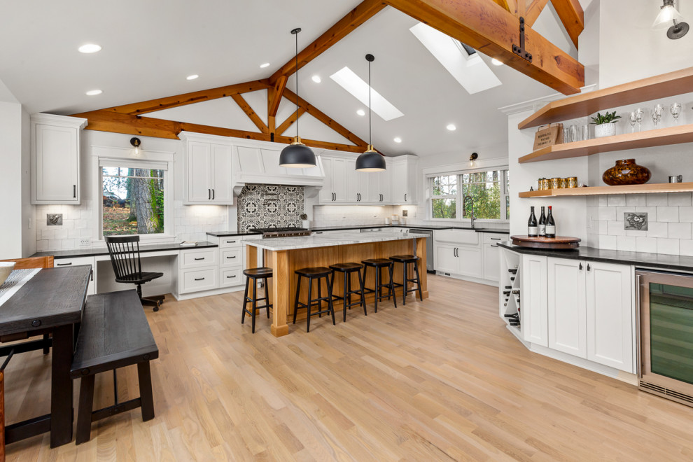 Design ideas for a country eat-in kitchen in Portland with a farmhouse sink, shaker cabinets, white cabinets, soapstone benchtops, white splashback, subway tile splashback, stainless steel appliances, light hardwood floors, with island, black benchtop and vaulted.