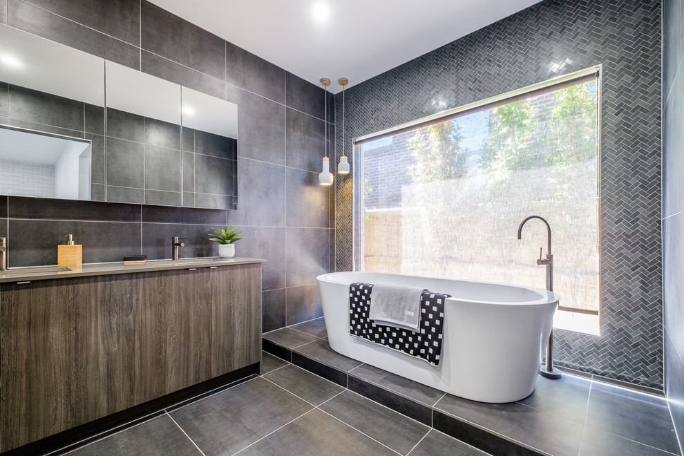 Photo of a contemporary 3/4 bathroom in Geelong with flat-panel cabinets, light wood cabinets, a freestanding tub, gray tile, grey walls, an undermount sink and grey floor.