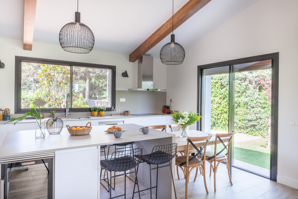 Large contemporary l-shaped open plan kitchen in Madrid with an undermount sink, flat-panel cabinets, white cabinets, quartz benchtops, beige splashback, engineered quartz splashback, stainless steel appliances, porcelain floors, with island, brown floor, beige benchtop and exposed beam.