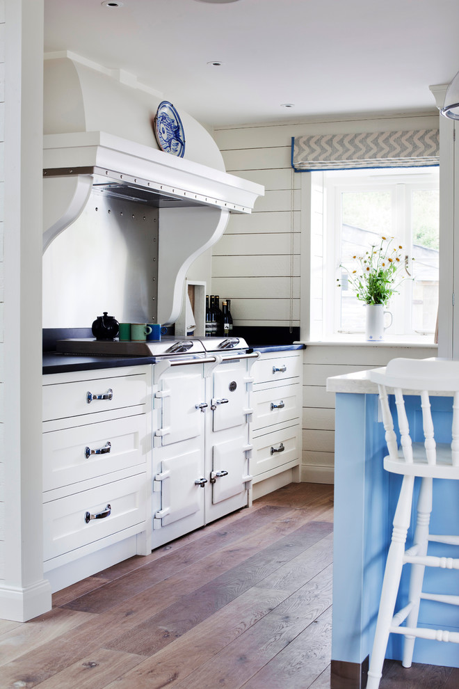 Design ideas for a beach style kitchen in Wiltshire with a farmhouse sink, recessed-panel cabinets, white cabinets, panelled appliances, quartz benchtops, medium hardwood floors, with island and brown floor.