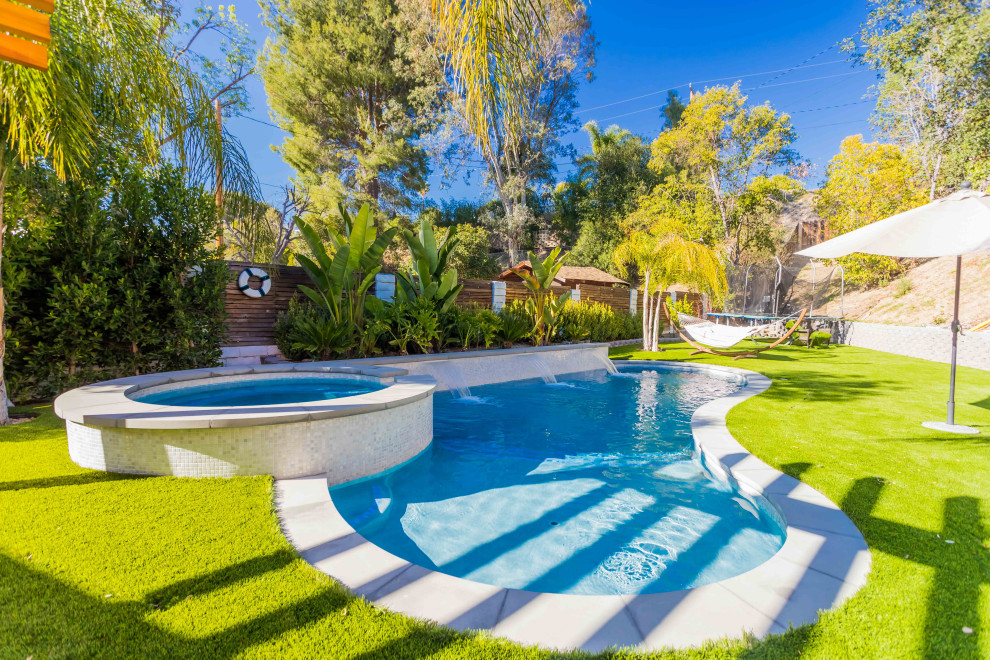 На фото: естественный ландшафтный бассейн среднего размера, в форме фасоли на заднем дворе в средиземноморском стиле с покрытием из бетонных плит