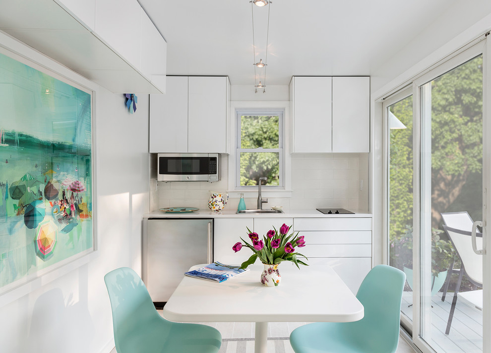 Inspiration for a beach style single-wall eat-in kitchen in New York with a single-bowl sink, flat-panel cabinets, white cabinets, white splashback and stainless steel appliances.