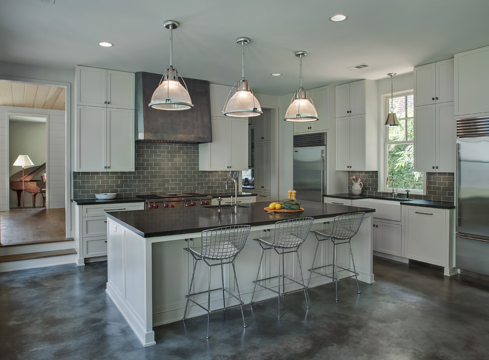 Inspiration for a mid-sized transitional l-shaped separate kitchen in Houston with a farmhouse sink, shaker cabinets, white cabinets, quartzite benchtops, grey splashback, subway tile splashback, stainless steel appliances, concrete floors, with island and grey floor.