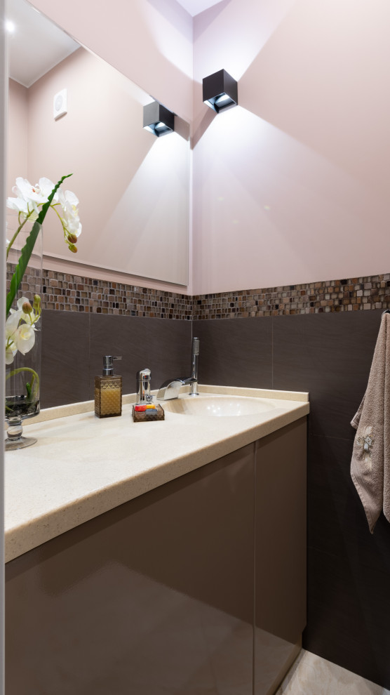 На фото: туалет среднего размера в стиле неоклассика (современная классика) с плоскими фасадами, коричневыми фасадами, инсталляцией, коричневой плиткой, удлиненной плиткой, розовыми стенами, полом из керамогранита, монолитной раковиной, столешницей из искусственного камня, коричневым полом, бежевой столешницей, встроенной тумбой и балками на потолке