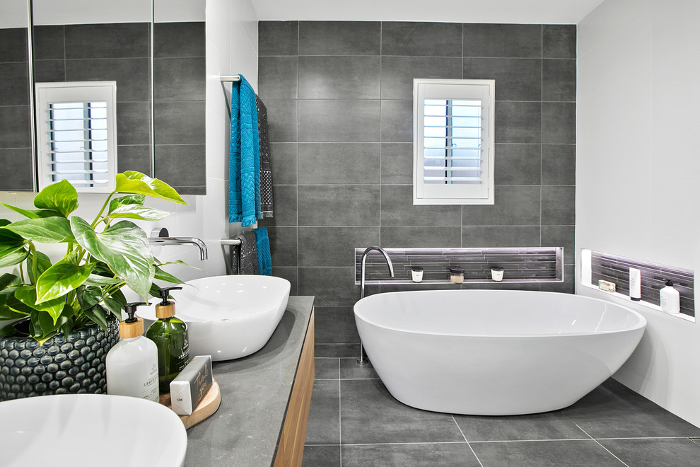 Inspiration for a mid-sized contemporary master wet room bathroom in Sydney with furniture-like cabinets, medium wood cabinets, a freestanding tub, a one-piece toilet, white tile, ceramic tile, grey walls, ceramic floors, a vessel sink, engineered quartz benchtops, grey floor, an open shower and grey benchtops.