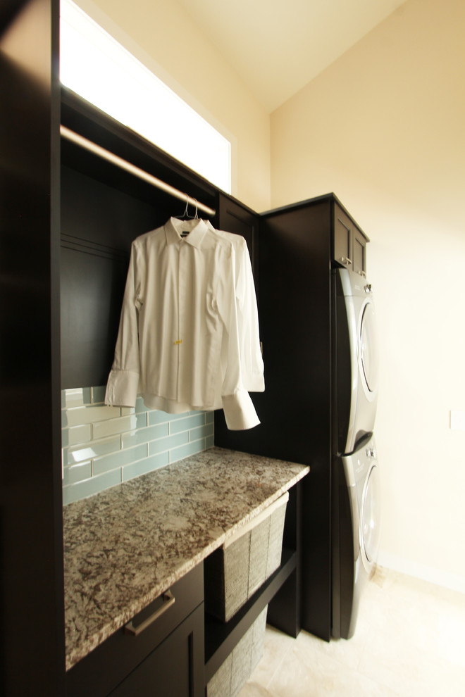 This is an example of a small transitional single-wall utility room in Other with recessed-panel cabinets, dark wood cabinets, granite benchtops, beige walls, travertine floors, a side-by-side washer and dryer, beige floor and beige benchtop.