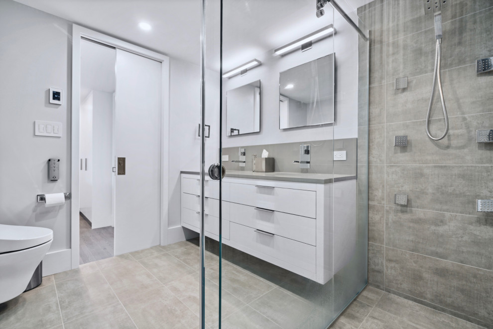 Пример оригинального дизайна: главная, серо-белая ванная комната среднего размера в современном стиле с плоскими фасадами, белыми фасадами, душем без бортиков, инсталляцией, серой плиткой, керамической плиткой, серыми стенами, полом из цементной плитки, врезной раковиной, столешницей из искусственного кварца, серым полом, душем с раздвижными дверями, серой столешницей, фартуком, тумбой под две раковины и подвесной тумбой
