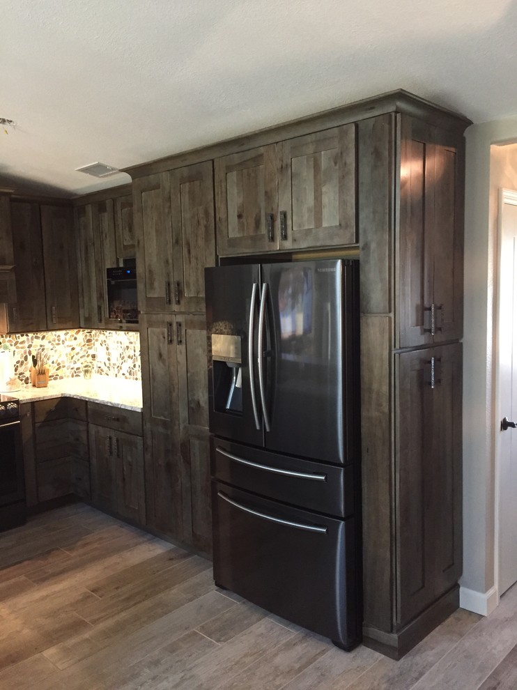 This is an example of a mid-sized beach style u-shaped eat-in kitchen in Cleveland with an undermount sink, shaker cabinets, distressed cabinets, quartzite benchtops, multi-coloured splashback, stone tile splashback, black appliances, porcelain floors and a peninsula.