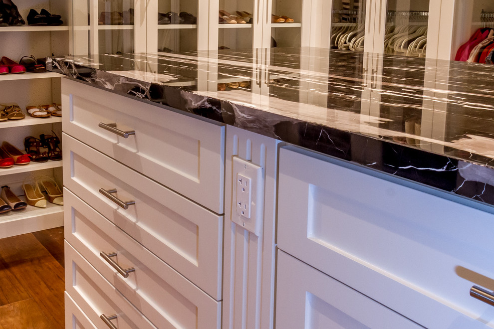 Inspiration for a large transitional gender-neutral walk-in wardrobe in Houston with glass-front cabinets, white cabinets and medium hardwood floors.