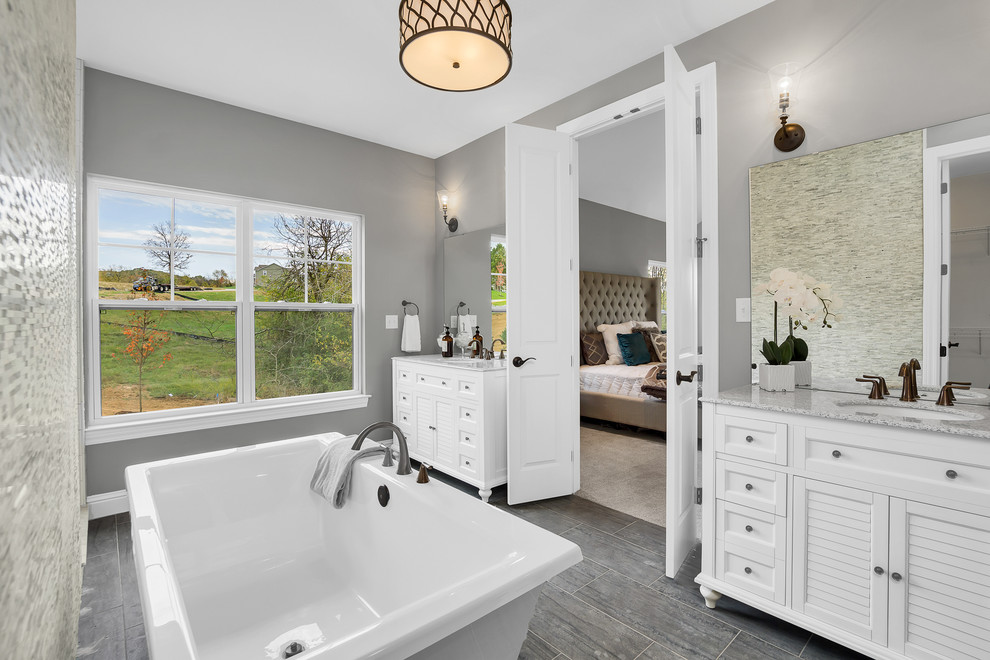 Inspiration for a country master bathroom in St Louis with a freestanding tub, ceramic tile, multi-coloured walls, ceramic floors, granite benchtops, louvered cabinets, white cabinets, an undermount sink and grey floor.
