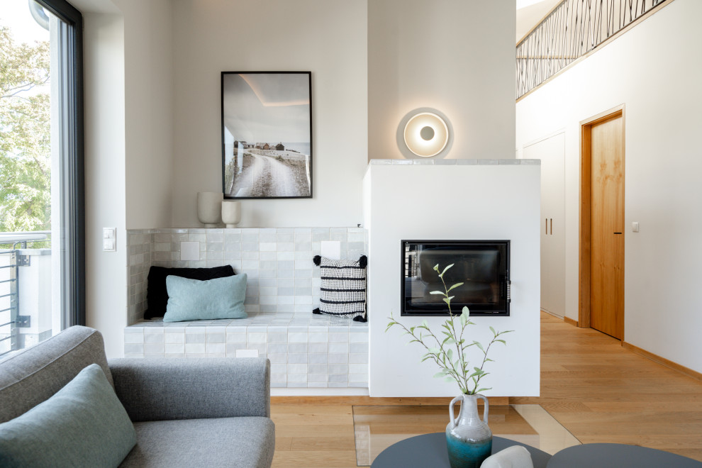 Mittelgroßes Skandinavisches Wohnzimmer in grau-weiß mit grauer Wandfarbe, hellem Holzboden, Kaminofen, verputzter Kaminumrandung und beigem Boden in Sonstige