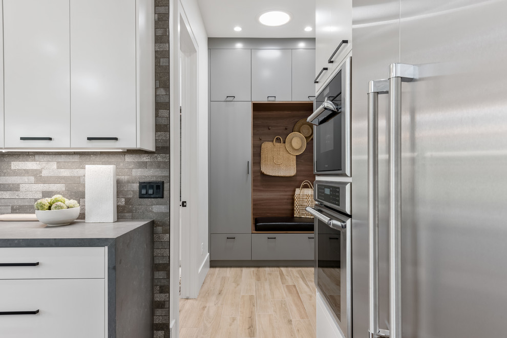 This is an example of a large contemporary l-shaped eat-in kitchen in Salt Lake City with a farmhouse sink, flat-panel cabinets, white cabinets, quartzite benchtops, grey splashback, stone tile splashback, stainless steel appliances, porcelain floors, with island, beige floor and grey benchtop.