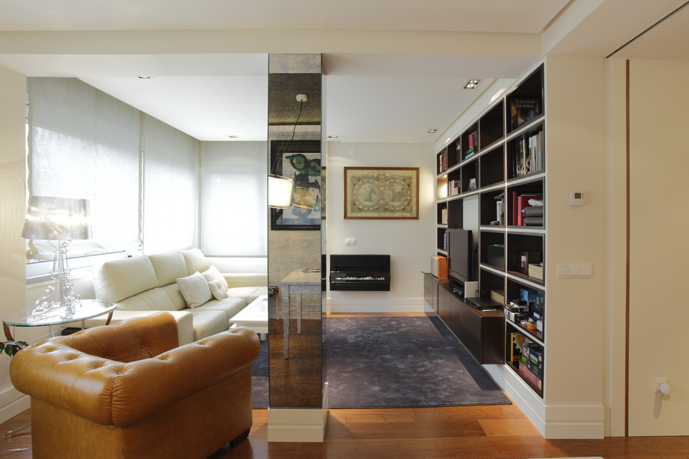 This is an example of a contemporary living room in Madrid with a library, medium hardwood floors and a built-in media wall.
