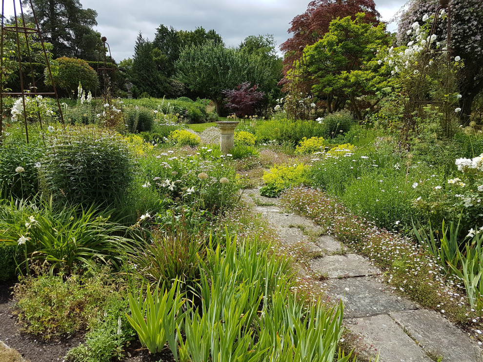 Kleiner Landhaus Garten im Sommer, hinter dem Haus mit Blumenbeet, direkter Sonneneinstrahlung und Natursteinplatten in Hampshire