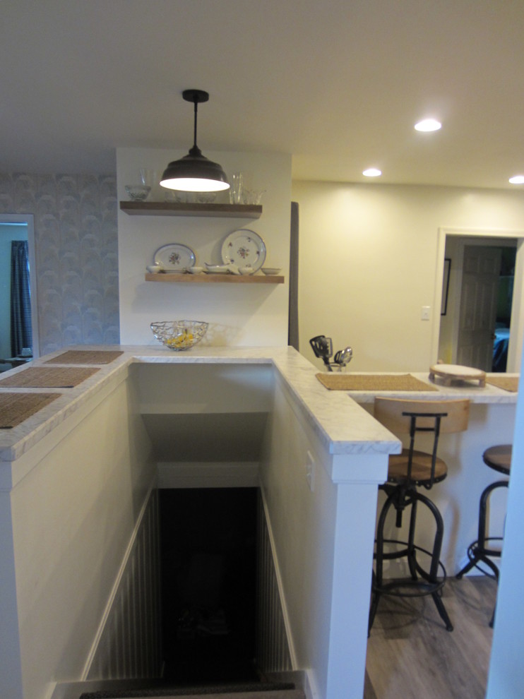 This is an example of a small country l-shaped eat-in kitchen in Louisville with a single-bowl sink, shaker cabinets, white cabinets, laminate benchtops, white splashback, ceramic splashback, black appliances, laminate floors, a peninsula, grey floor and white benchtop.