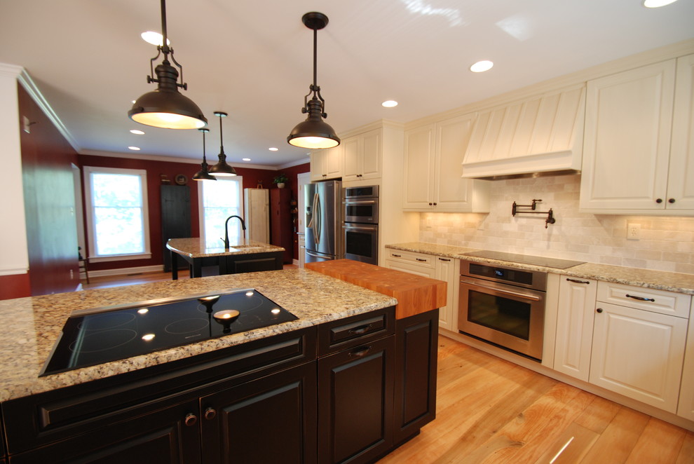Mid-sized traditional l-shaped separate kitchen in DC Metro with a farmhouse sink, raised-panel cabinets, white cabinets, granite benchtops, white splashback, porcelain splashback, stainless steel appliances, light hardwood floors, multiple islands, brown floor and beige benchtop.