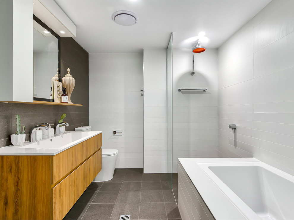 This is an example of a contemporary bathroom in Brisbane with flat-panel cabinets, light wood cabinets, a drop-in tub, a curbless shower, gray tile, white tile, white walls, a trough sink, grey floor and an open shower.